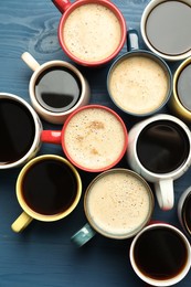 Many cups of different coffee drinks on blue wooden table, flat lay