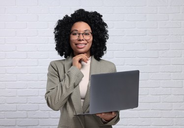 Photo of Young businesswoman using laptop near white brick wall