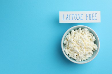 Photo of Cottage cheese and card with phrase Lactose free on light blue table, top view. Space for text