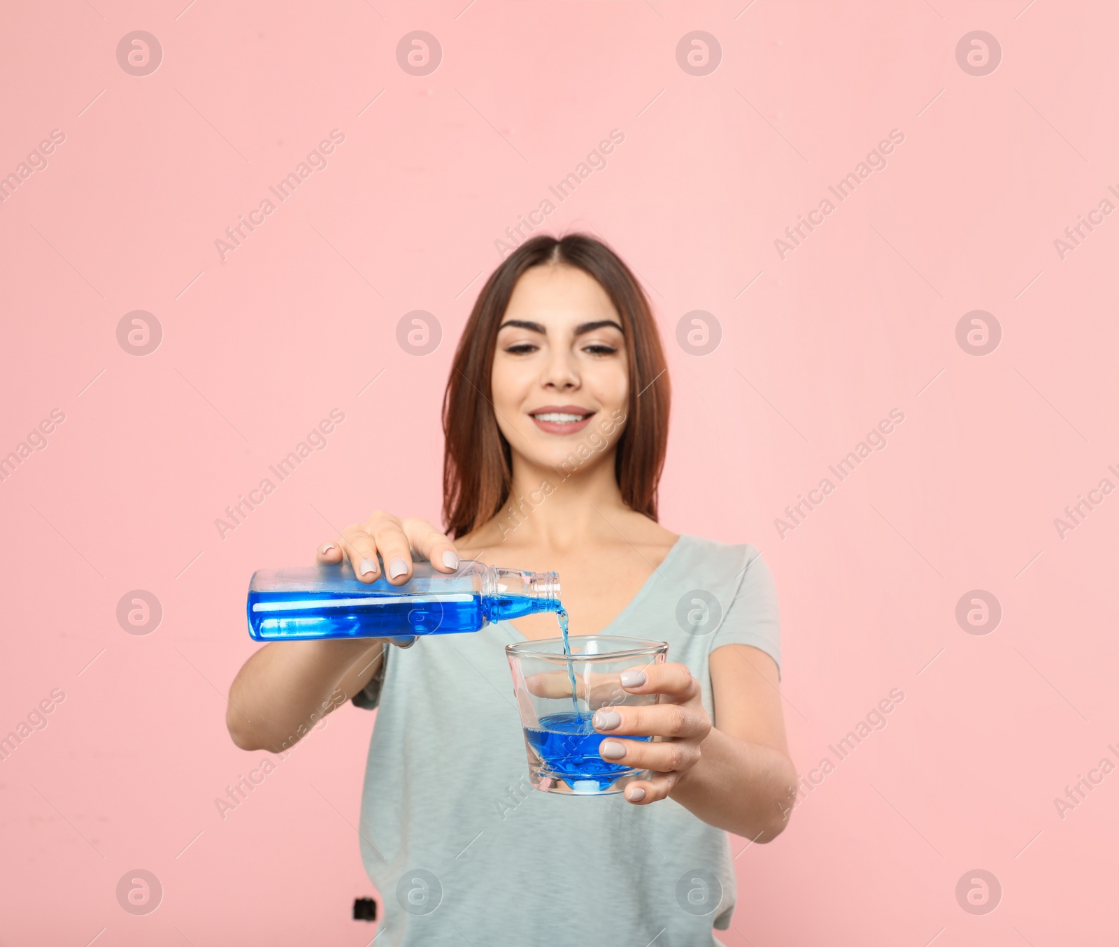 Photo of Beautiful woman pouring mouthwash from bottle into glass on color background. Teeth and oral care