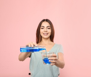 Photo of Beautiful woman pouring mouthwash from bottle into glass on color background. Teeth and oral care