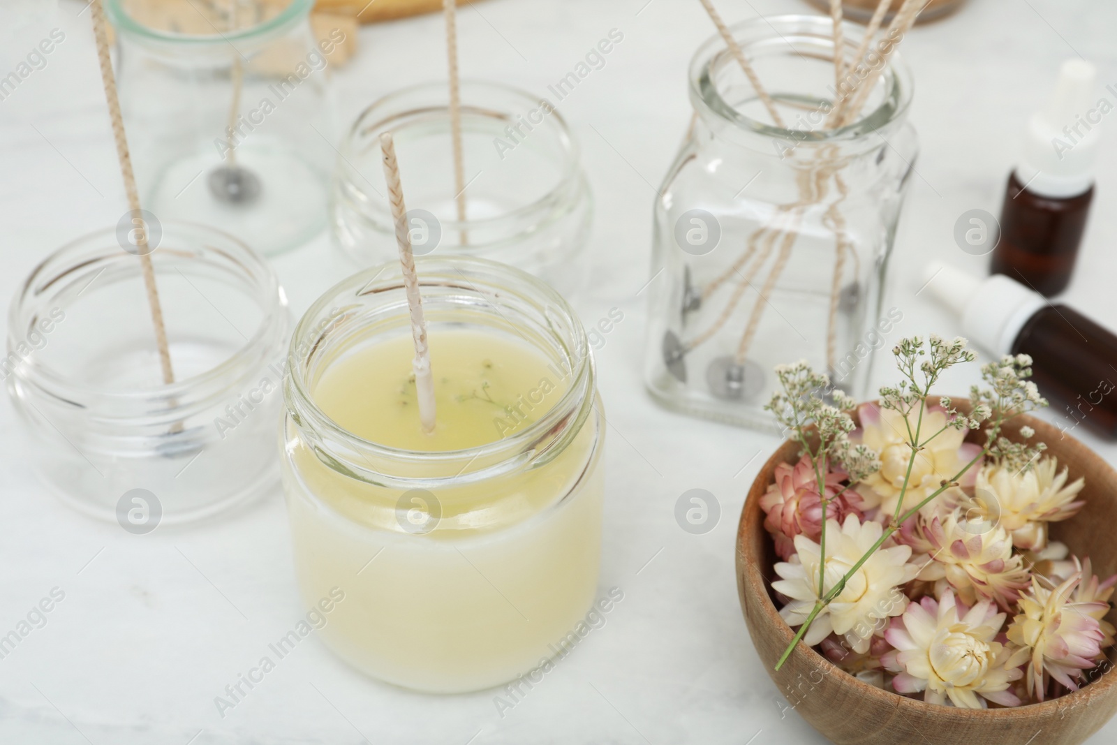 Photo of Glass jar with wax, wick and flowers on white table. Making homemade candle