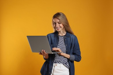 Portrait of young woman with modern laptop on yellow background