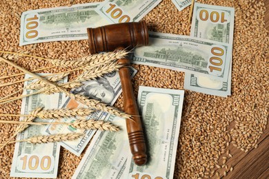 Photo of Dollar banknotes, judge's gavel, wheat ears and grains on wooden table, top view. Agricultural business