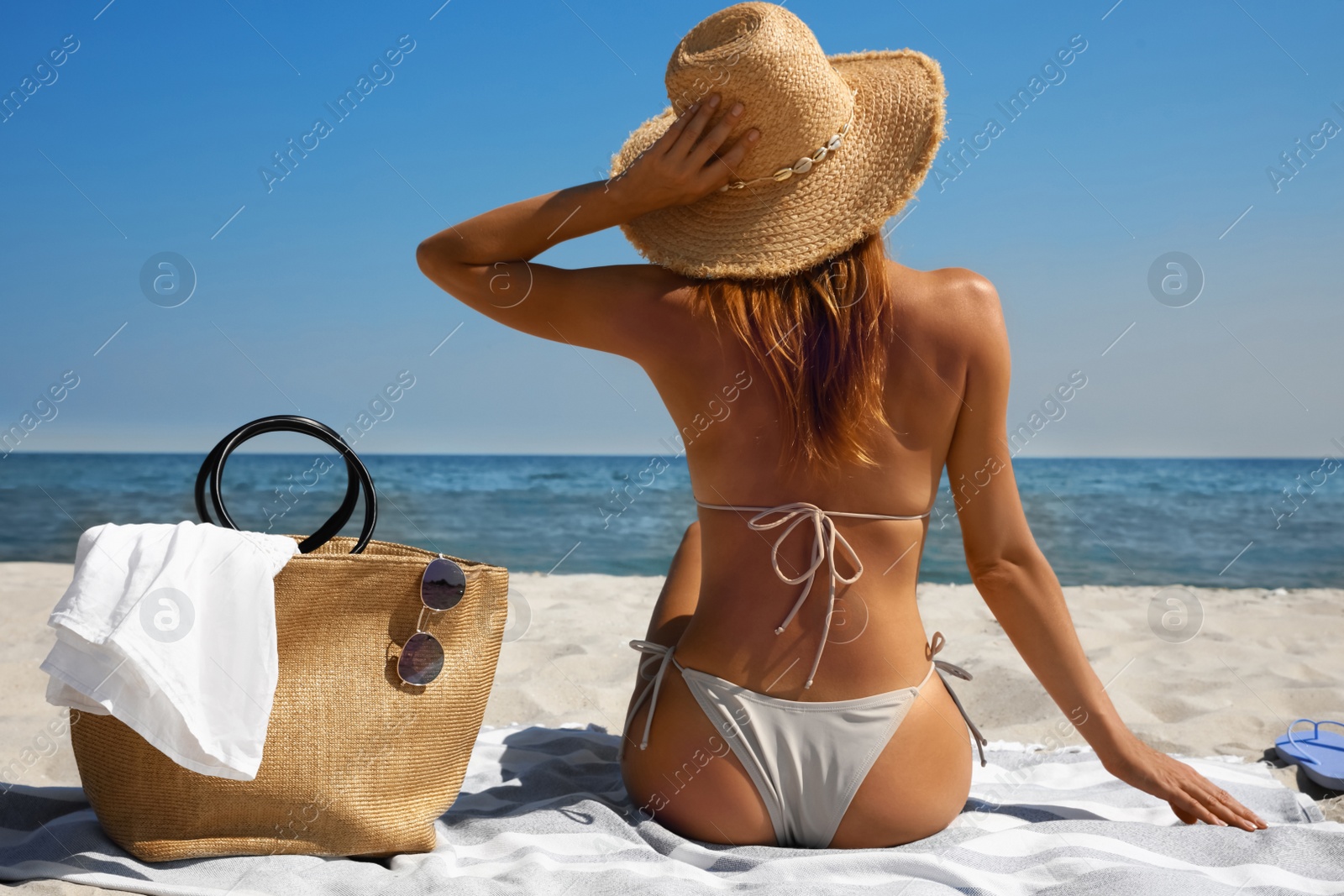 Photo of Woman with beach bag and straw hat on sand near sea, back view