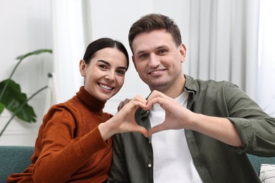 Happy couple making heart with hands at home