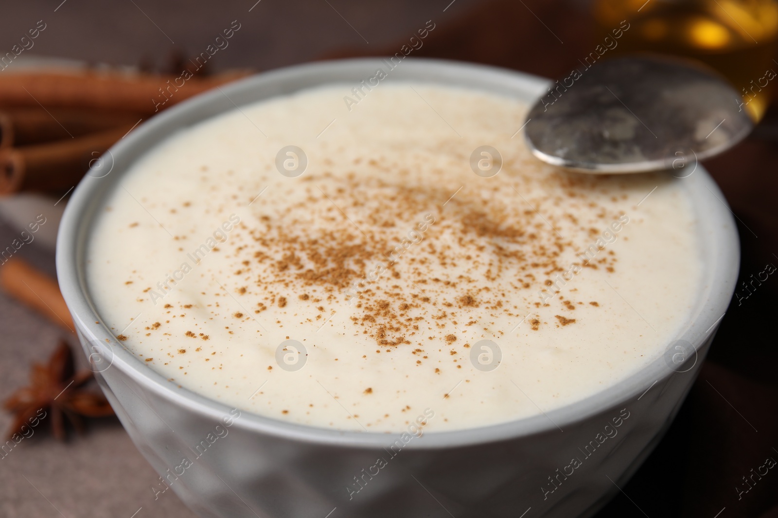 Photo of Delicious semolina pudding with cinnamon in bowl and spoon on table, closeup