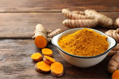 Bowl with aromatic turmeric powder and cut roots on wooden table. Space for text