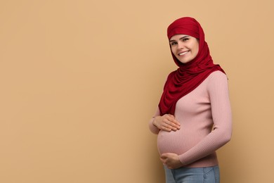 Portrait of pregnant Muslim woman in hijab on beige background, space for text