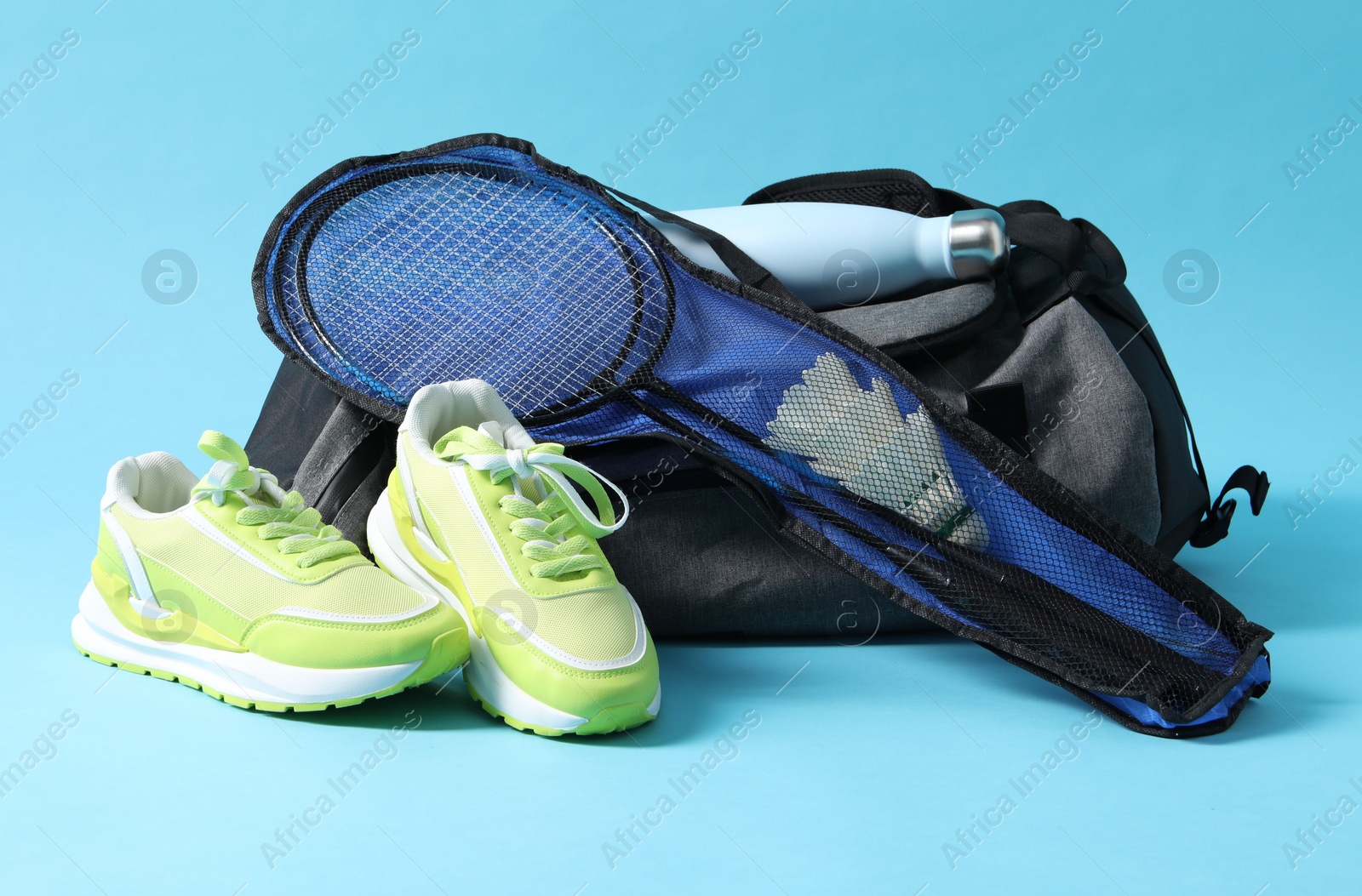 Photo of Badminton set, bag, sneakers and bottle on light blue background