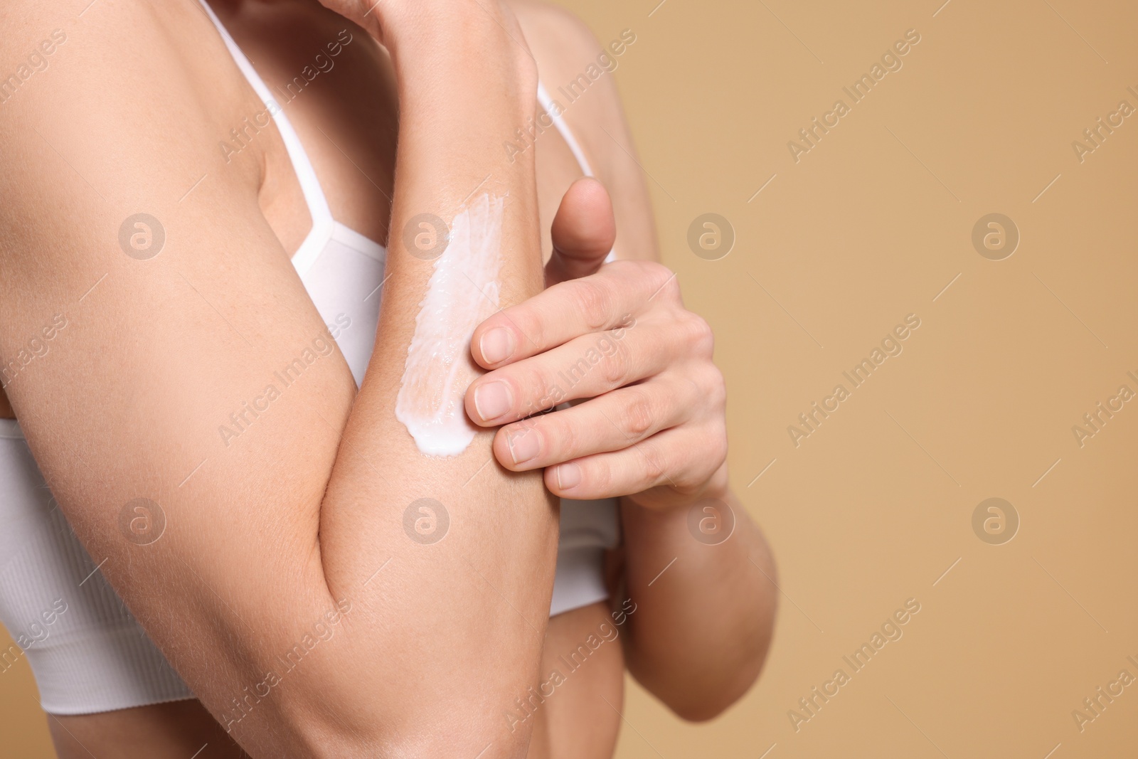 Photo of Woman applying body cream onto her arm against beige background, closeup. Space for text