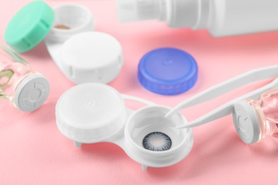 Photo of Cases with color contact lenses and tweezers on pink background