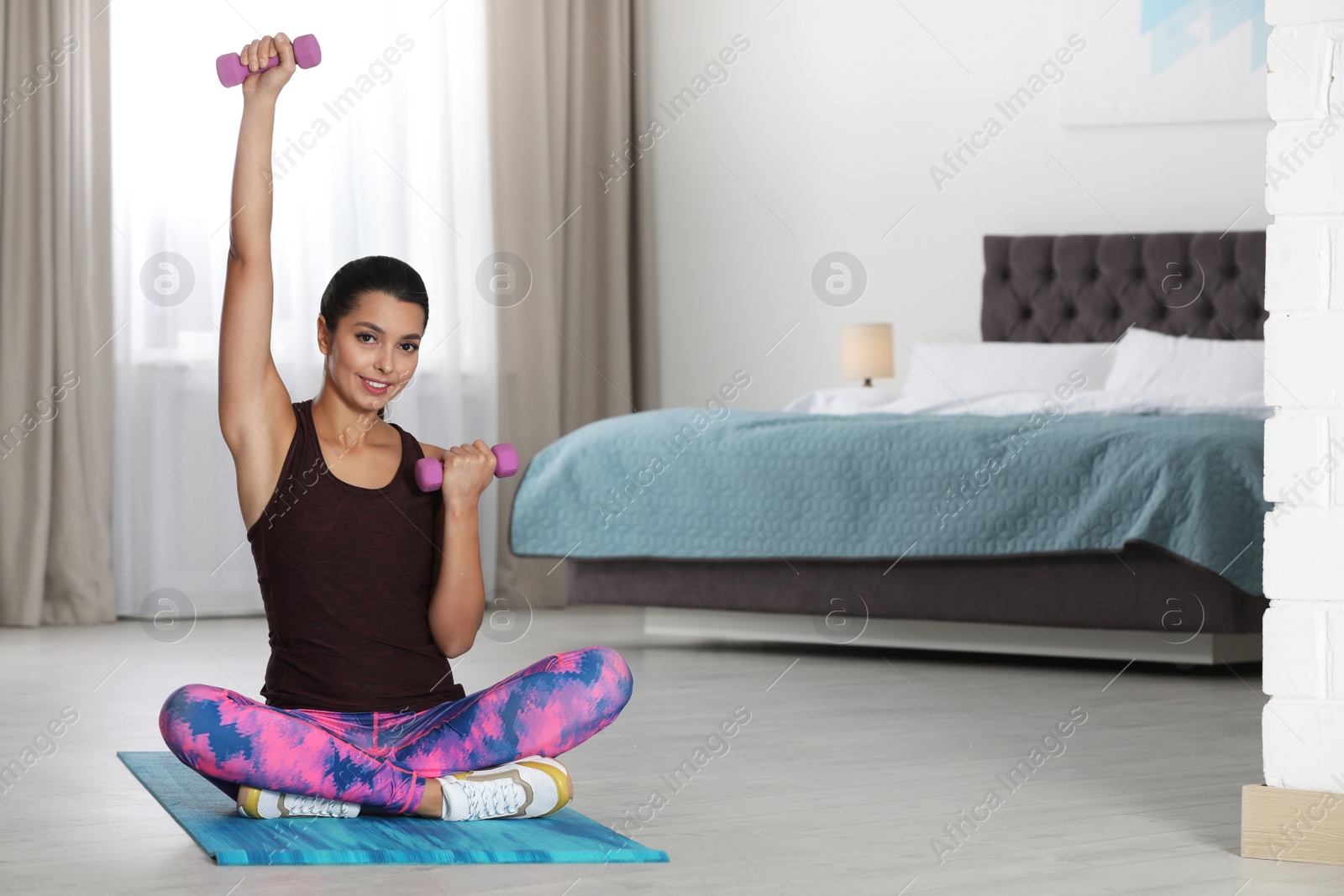 Photo of Young woman in fitness clothes doing exercise with dumbbells at home. Space for text