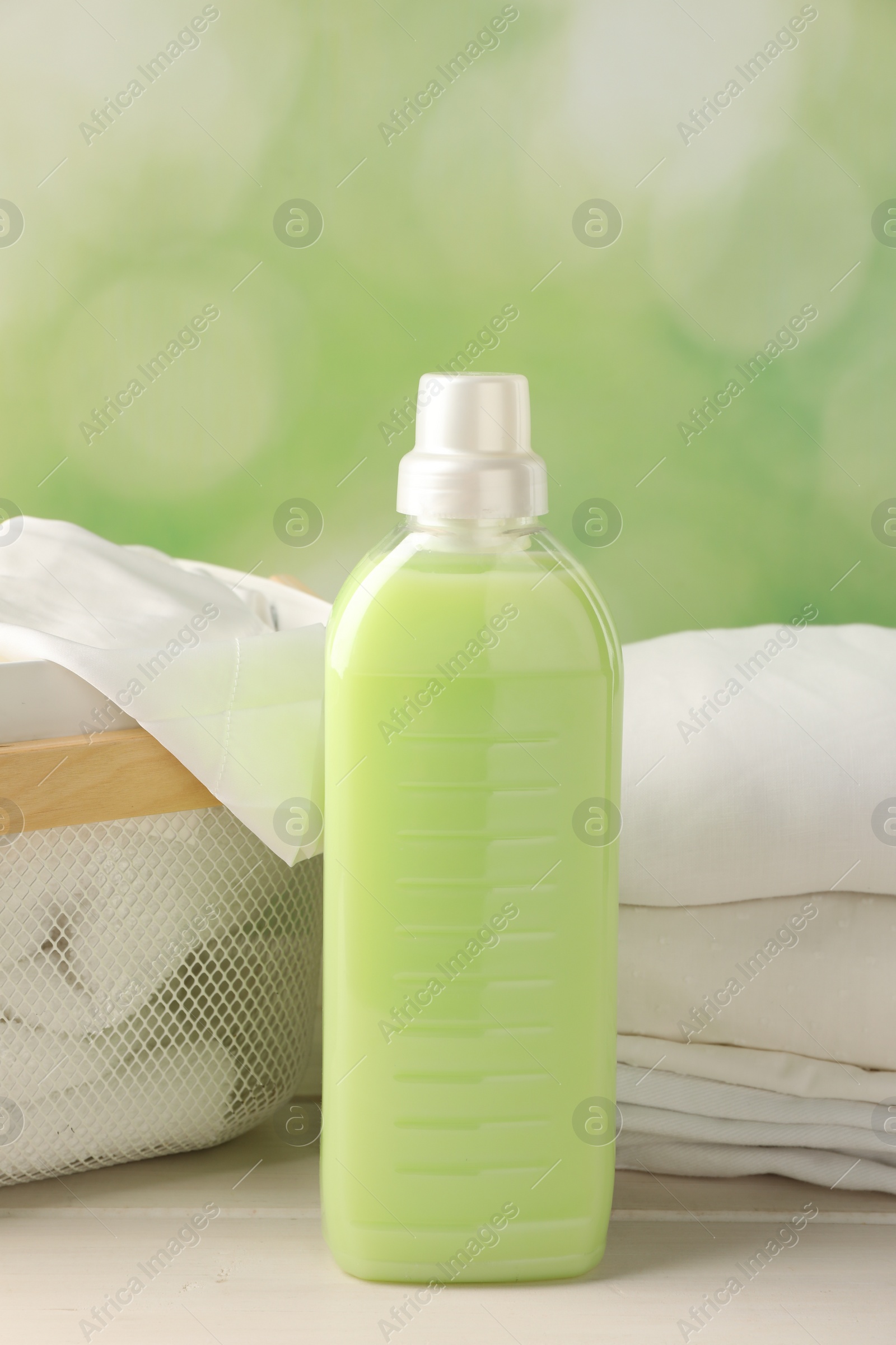 Photo of Bottle of laundry detergent and clean clothes on white wooden table