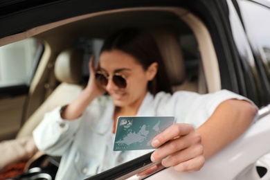 Photo of Woman sitting in car and showing credit card at gas station, focus on hand