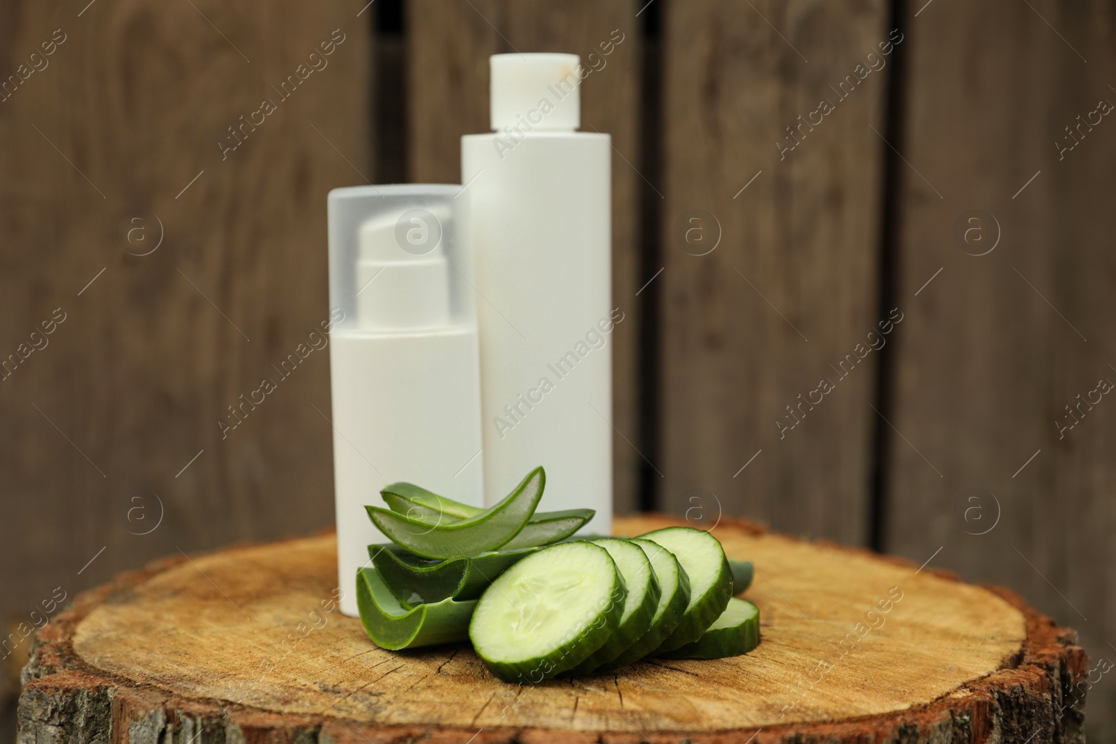 Photo of Bottles of cosmetic products, sliced aloe vera leaves and cucumber on wooden stump