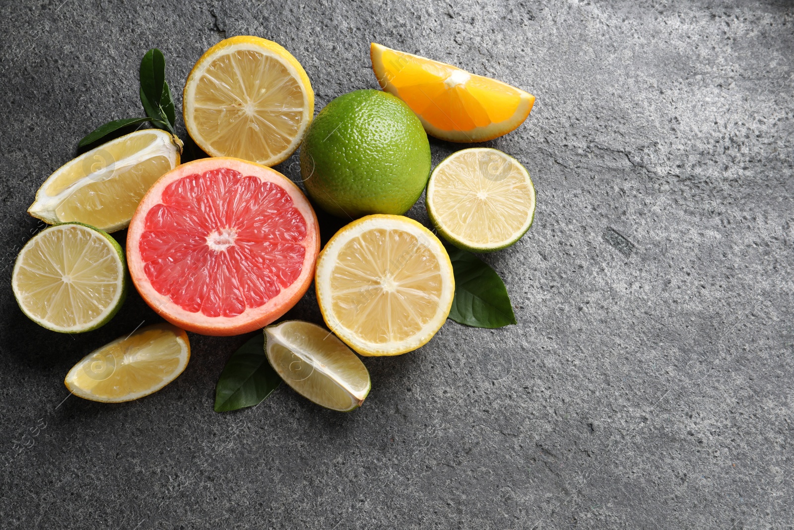 Photo of Different fresh citrus fruits and leaves on grey textured table, flat lay. Space for text