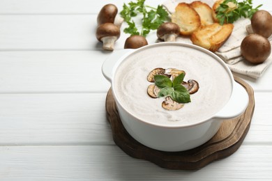 Delicious homemade mushroom soup in ceramic pot, croutons, fresh champignons and parsley on white wooden table. Space for text