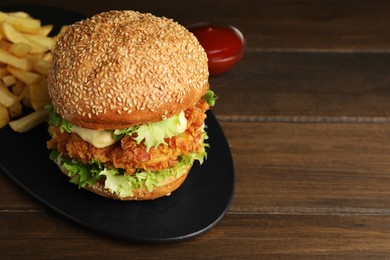 Photo of Delicious burger with crispy chicken patty, french fries and sauce on wooden table. Space for text