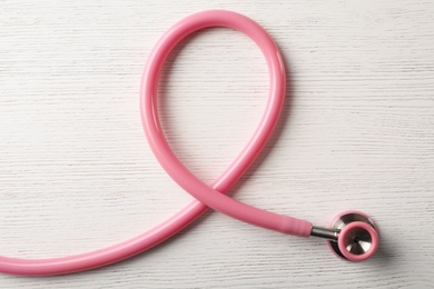 Pink stethoscope folded like awareness ribbon on wooden background, top view. Breast cancer concept