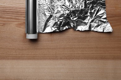 Photo of Roll of aluminum foil on wooden table, top view. Space for text