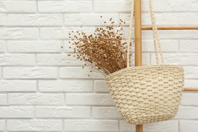 Photo of Stylish beach bag with beautiful dried flowers hanging  on wooden ladder. Space for text