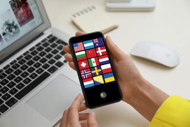 Translator using smartphone with images of different flags on screen at table, closeup