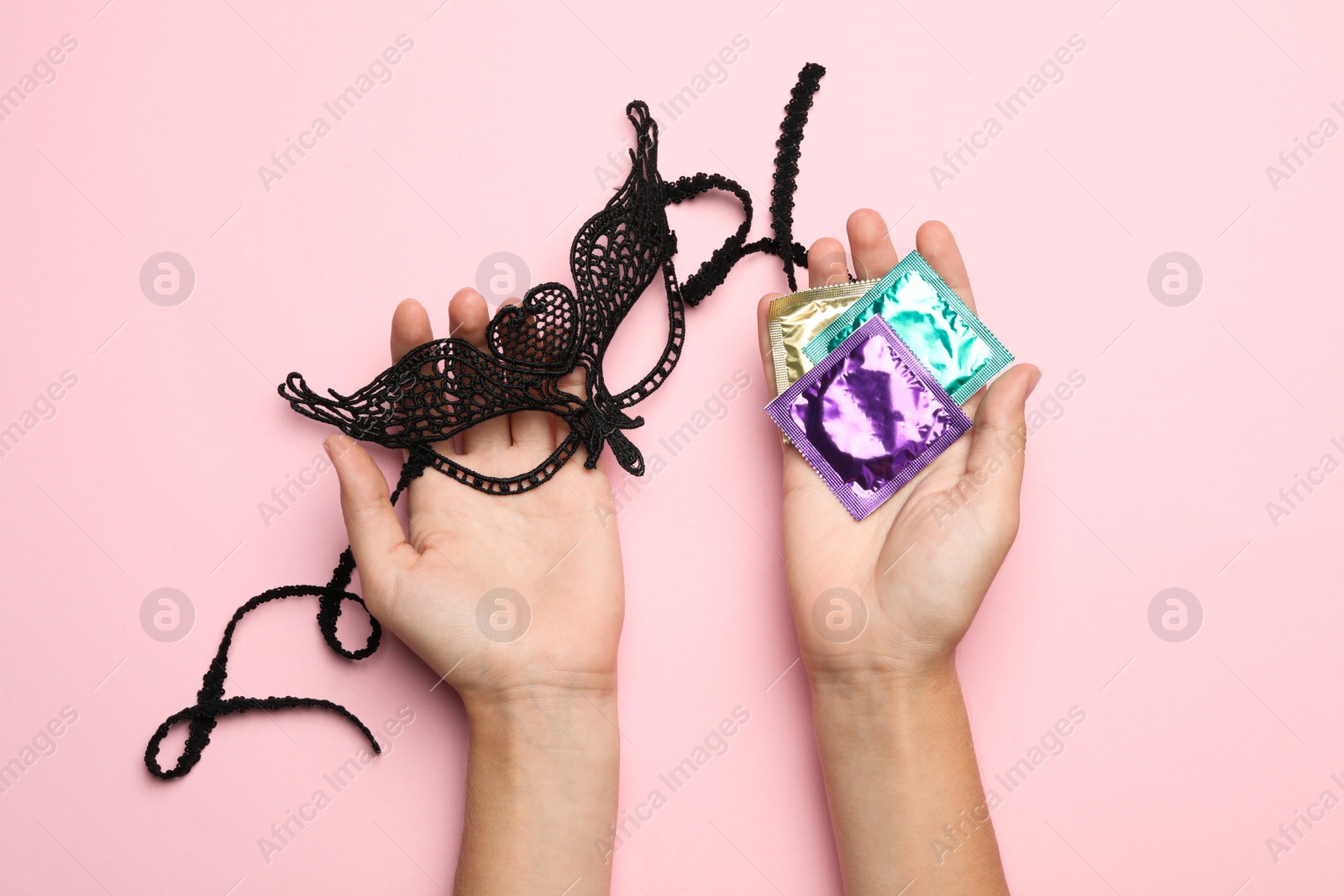 Photo of Woman with lace mask and condoms on pink background, top view. Sex game