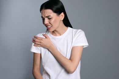 Woman suffering from shoulder pain on grey background