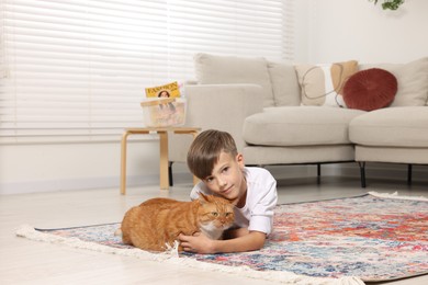 Little boy petting cute ginger cat on carpet at home