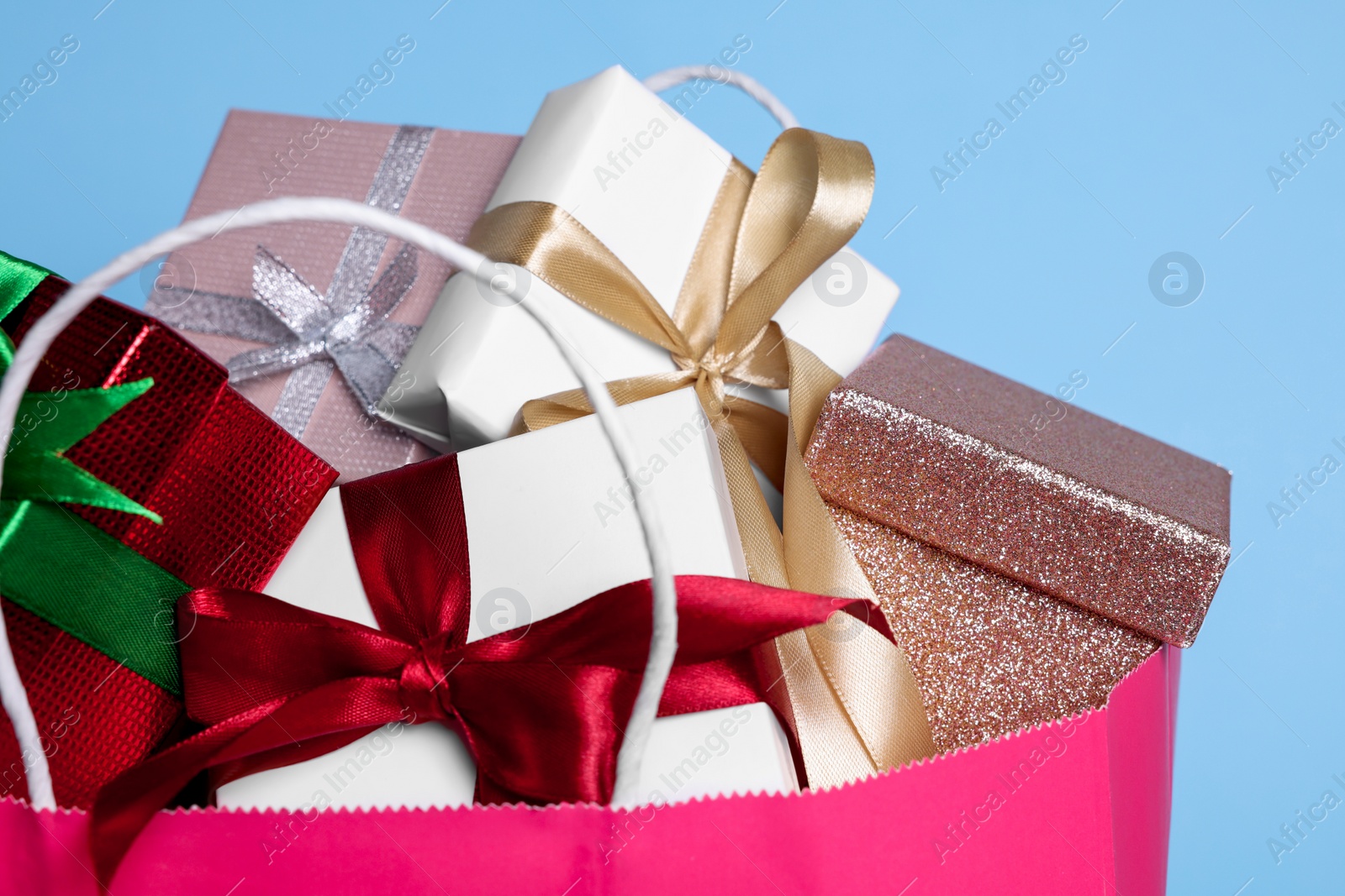 Photo of Pink paper shopping bag full of gift boxes on light blue background, closeup
