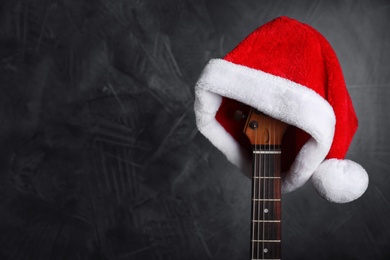 Photo of Guitar with Santa hat on black background, space for text. Christmas music