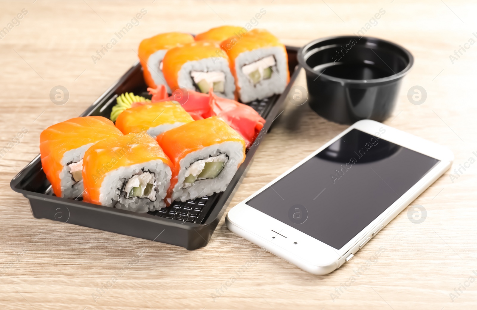 Photo of Smartphone with space for text and sushi rolls served on wooden table. Food delivery