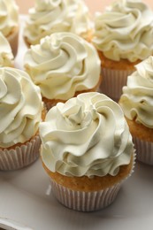 Photo of Tasty vanilla cupcakes with cream on plate, closeup