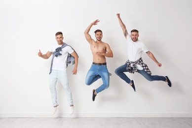 Group of young men in jeans jumping near light wall