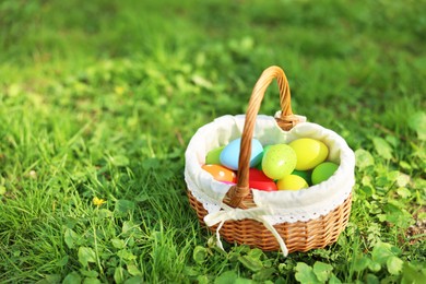 Photo of Easter celebration. Painted eggs in wicker basket on green grass, space for text