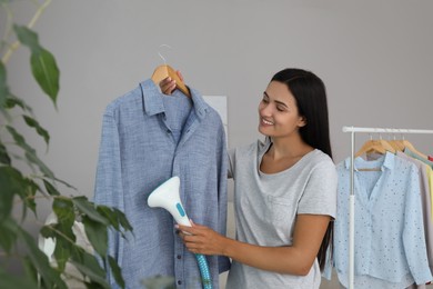 Photo of Woman steaming shirt on hanger at home