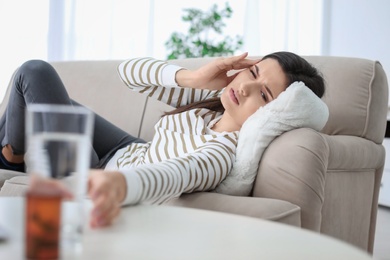 Photo of Young woman suffering from headache on sofa at home