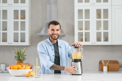 Photo of Handsome man preparing ingredients for tasty smoothie at white marble table in kitchen