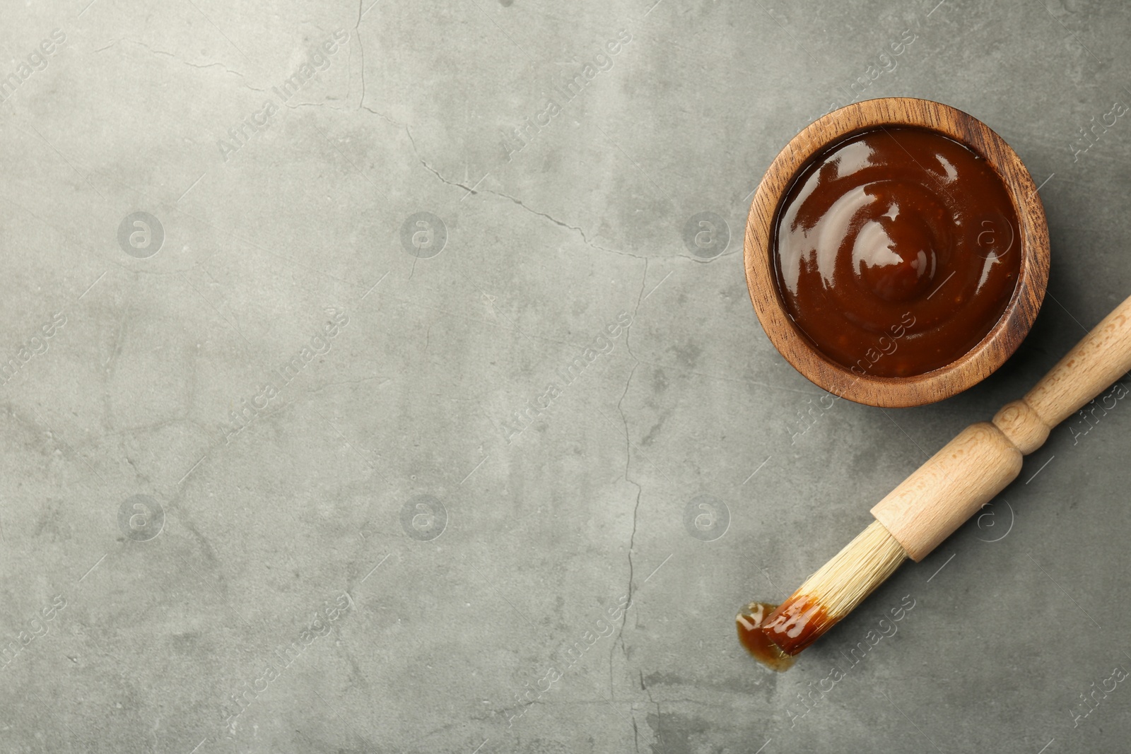 Photo of Tasty barbeque sauce in bowl and brush on grey textured table, top view. Space for text