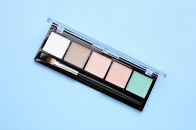 Photo of Contouring palette with brush on light blue background, top view. Professional cosmetic product