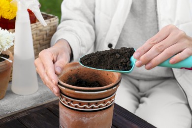 Photo of Woman adding fresh soil into pot in garden, closeup