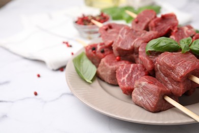Photo of Wooden skewers with cut fresh beef meat, basil leaves and spices on white table, closeup. Space for text