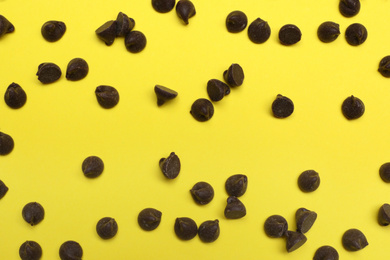 Delicious chocolate chips on yellow background, top view