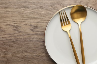 Photo of Plate, fork and spoon on wooden table, top view. Space for text