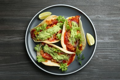 Delicious tacos with guacamole, meat and vegetables on wooden table, top view