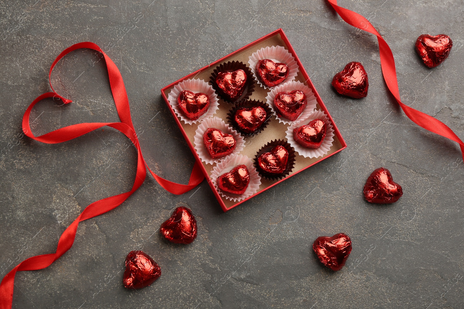 Photo of Heart shaped chocolate candies and ribbon on grey table, flat lay