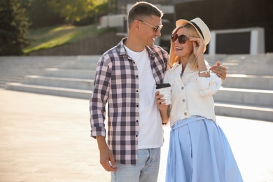 Happy couple with drink walking along city street on summer day