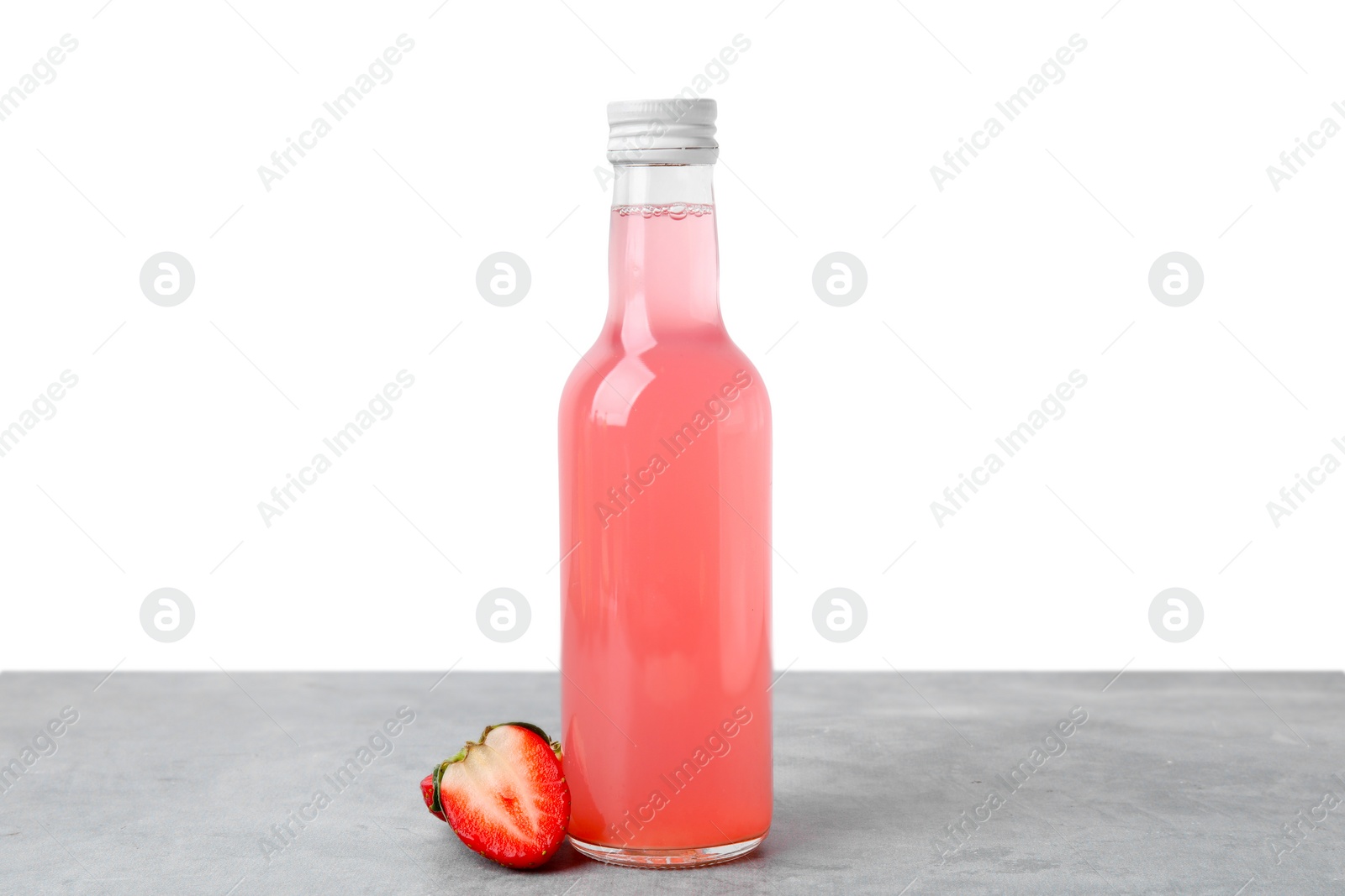 Photo of Delicious kombucha in glass bottle and strawberry on grey table against white background