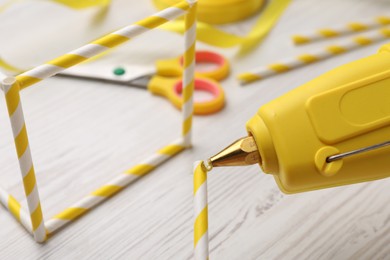 Photo of Making craft with hot glue gun and straws on white wooden table, closeup